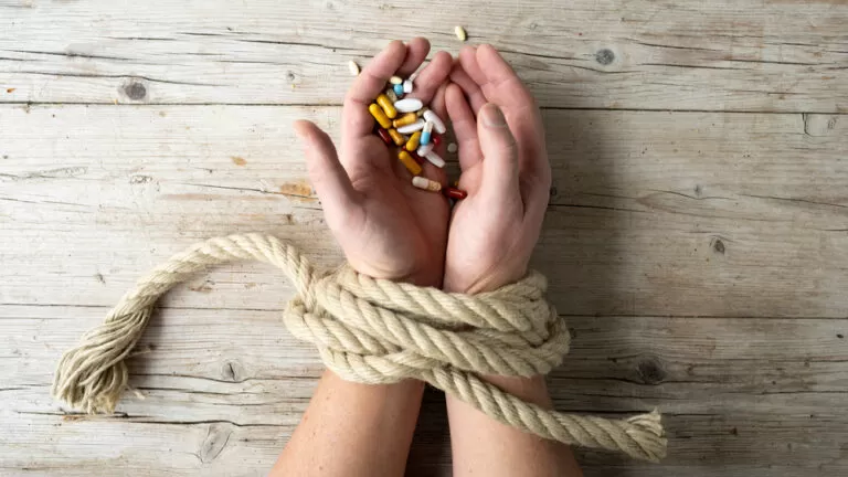Deze persoon heeft een medicijnen verslaving. Zijn handen zijn vastgebonden om niet de pillen te nemen. Hij kan hulp krijgen met zijn medicatie verslaving van Verslavingshulp Nederland.